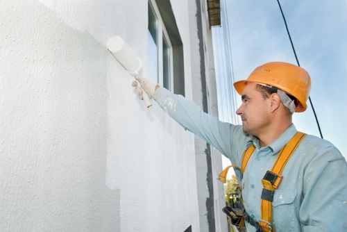 employee painting stucco on exterior of home