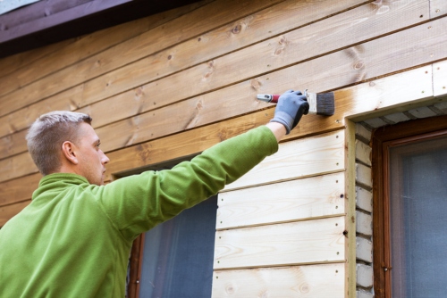 painter with paintbrush painting house wood siding